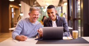 Zwei Männer im Gespräch am Laptop – Mentoring für Führungskräfte im Arbeitsalltag
