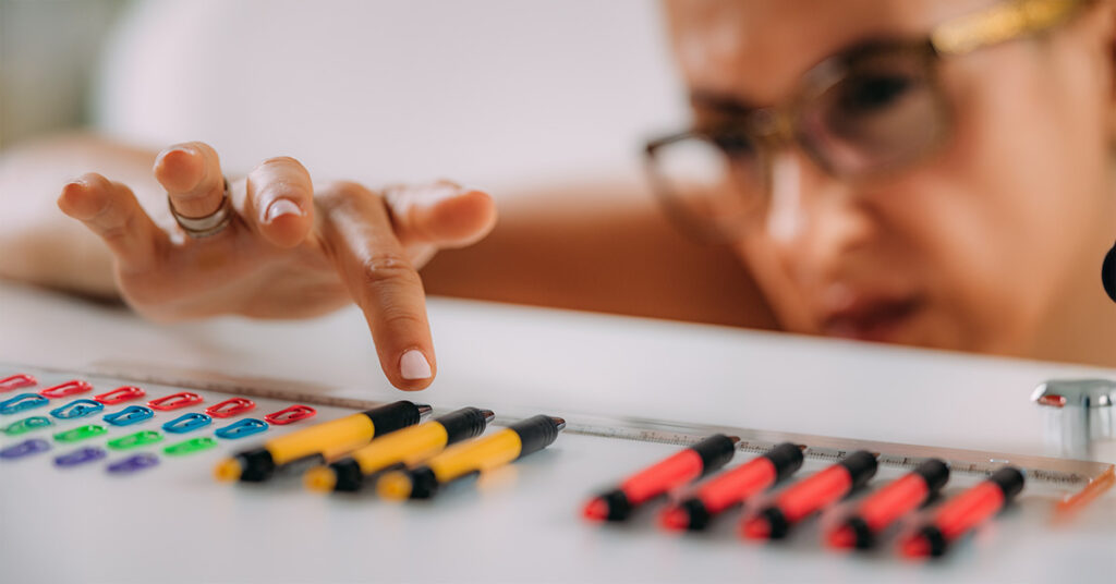 Frau ordnet akribisch Stifte und Büroklammern – Symbolbild für Perfektionismus im Arbeitsalltag und die Notwendigkeit, Perfektionismus zu überwinden.