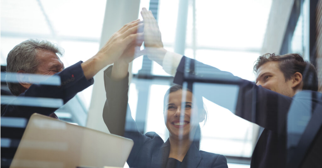 Drei Führungskräfte geben sich im Büro einen High-Five – Symbol für Vertrauen im Team und erfolgreiche Zusammenarbeit