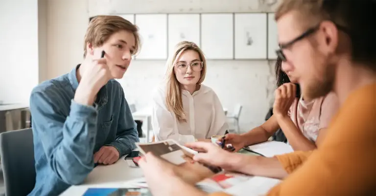 Junge Menschen sitzen im Team zusammen, diskutieren über Unterlagen und wirken konzentriert – ein Moment, der sinnbildlich für Fehlerkultur im Team steht.