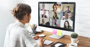 Eine Frau folgt an einem Computer einem virtuellen Meeting mit mehreren Kollegen.