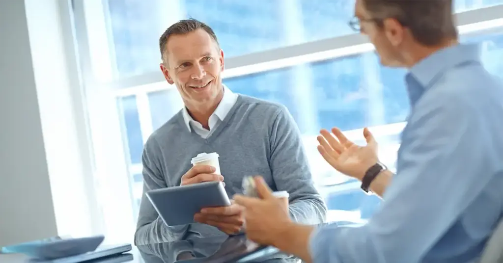 Führungskraft gibt Mitarbeiter-Feedback im Gespräch – zwei Männer im Business-Kontext unterhalten sich am Tisch über Zusammenarbeit und Ziele.