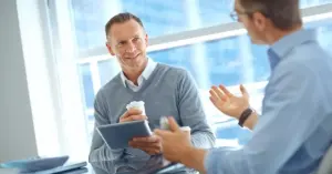 Führungskraft gibt Mitarbeiter-Feedback im Gespräch – zwei Männer im Business-Kontext unterhalten sich am Tisch über Zusammenarbeit und Ziele.