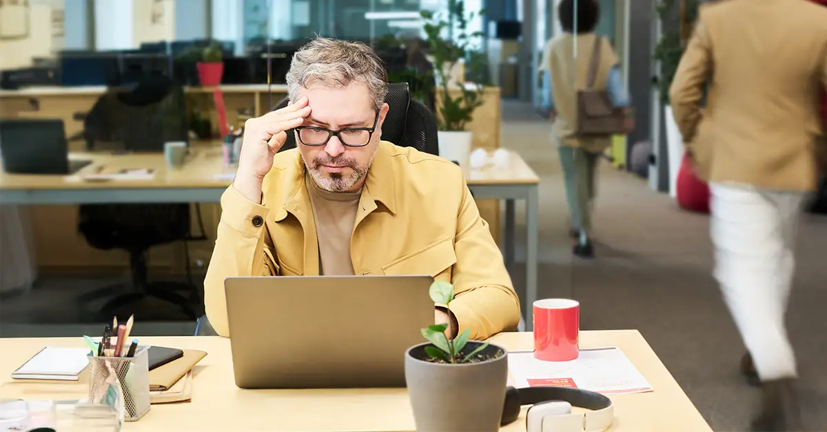 Nachdenklicher Manager am Arbeitsplatz vor dem Laptop, der frustriert wirkt, weil seine Leistung nicht anerkannt wird.