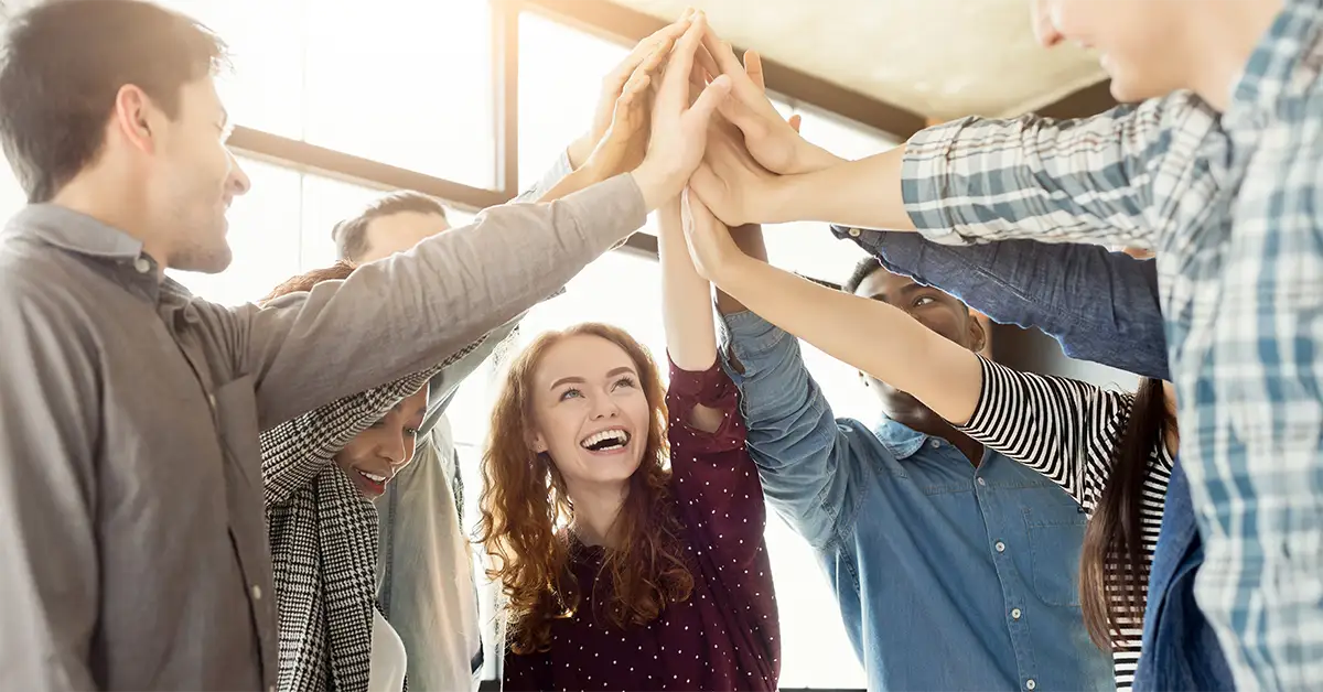 Eine Gruppe lächelnder Mitarbeitender steht im Kreis und gibt gemeinsam ein High-Five, als Symbol dafür, das Team zu stärken und Erfolge gemeinsam zu feiern.